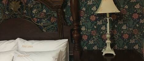 Una cama bien hecha con sábanas y almohadas blancas, con la etiqueta "Hotel screen". La habitación tiene papel tapiz floral y una mesita de noche de madera con una lámpara.