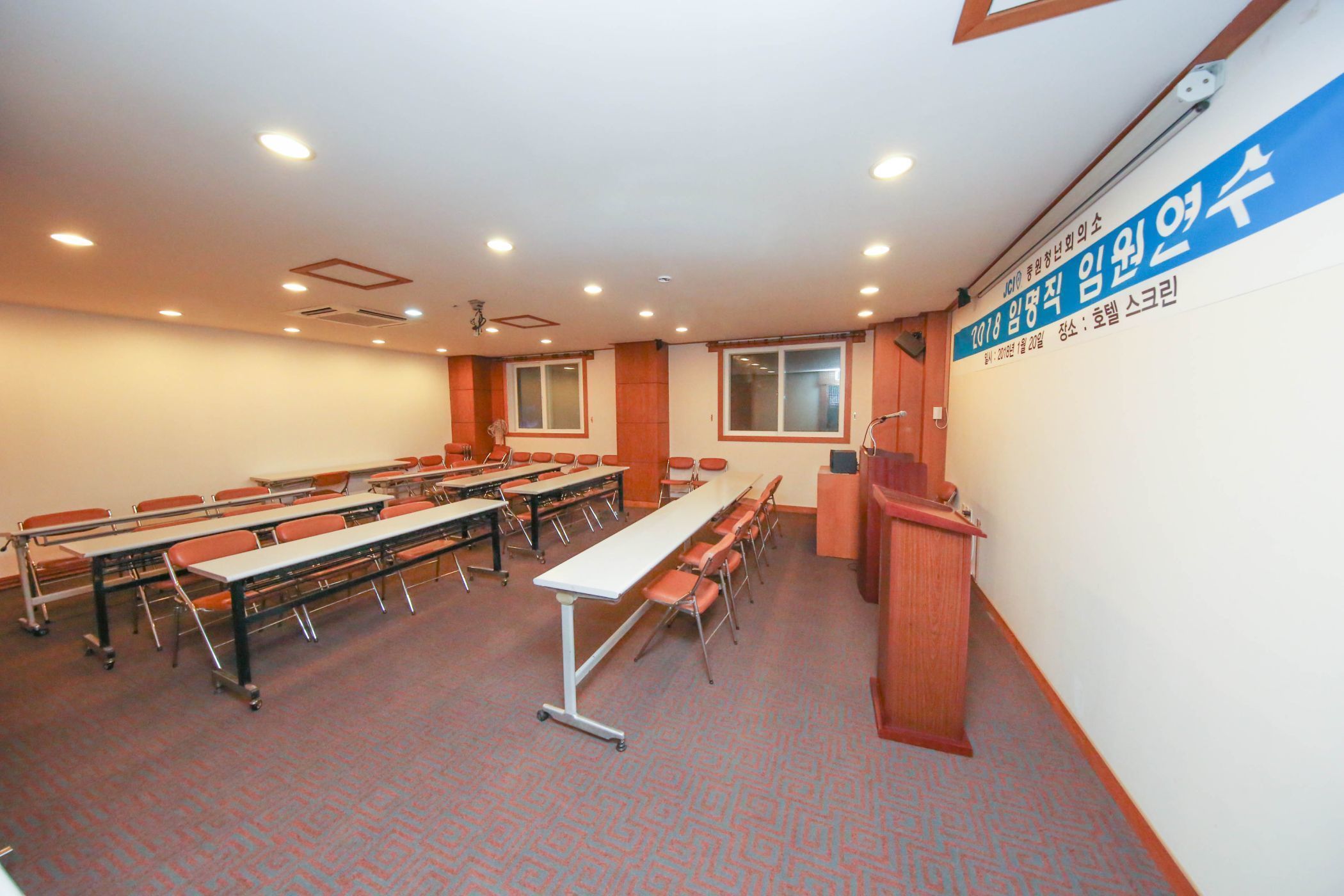 A conference room with tables and chairs, a podium, and a wall with text.