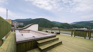 A wooden deck with a view of green hills and a building in the background. - Suanbo Hotel Screen (Chungju)
