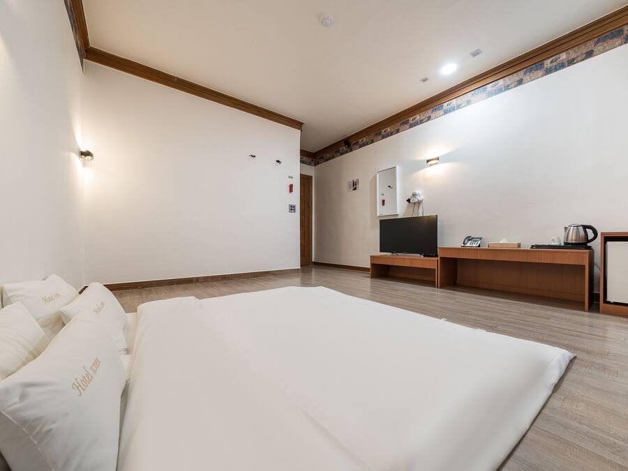 A hotel room with a large bed, a wooden desk, a television, and a mirror.