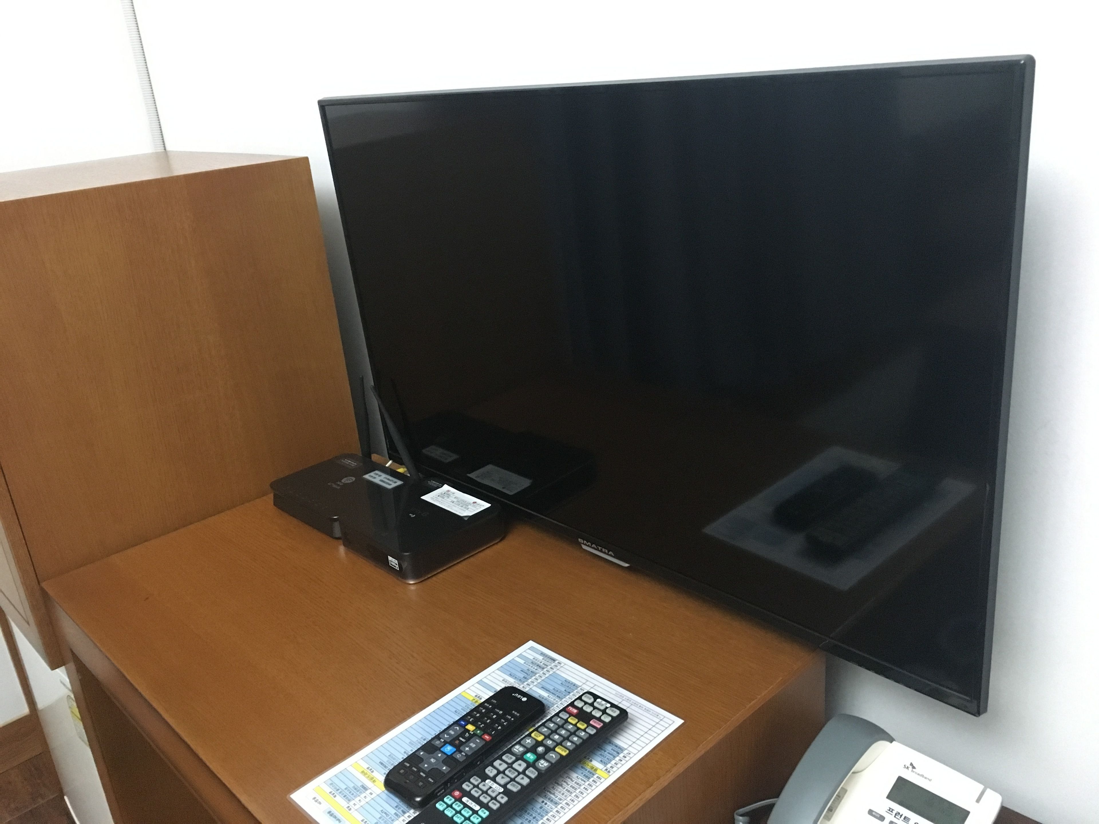 Un televisor sobre un soporte de madera, con un control remoto y una guía impresa en el soporte.