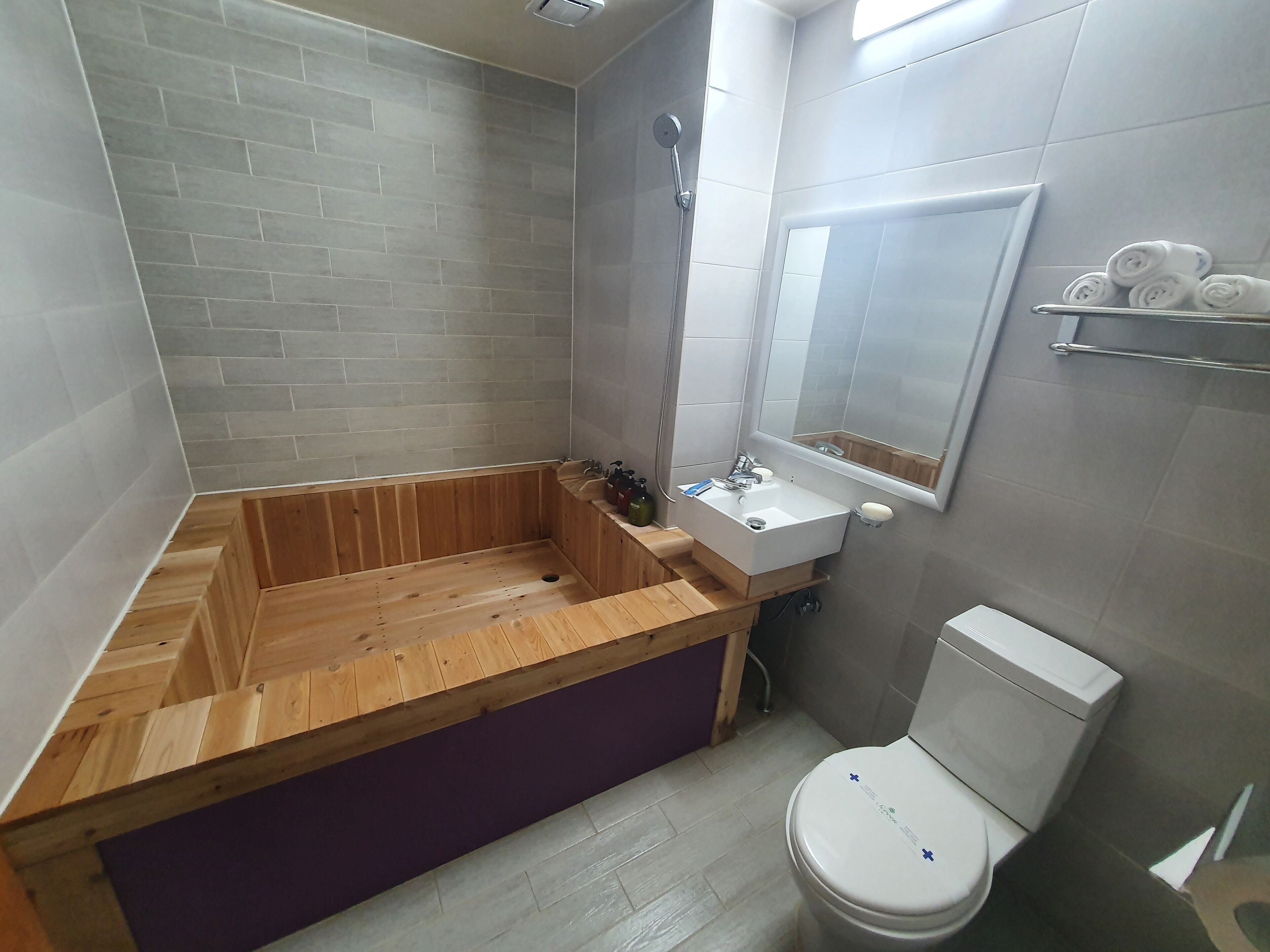 A bathroom with a wooden bathtub, a sink with a mirror, and a toilet.