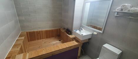 Un baño con una bañera de madera, un lavabo con espejo y un inodoro.