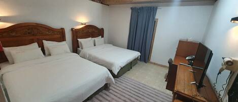 A hotel room with two beds, a wooden dresser, a desk with a computer, and a window with blue curtains.