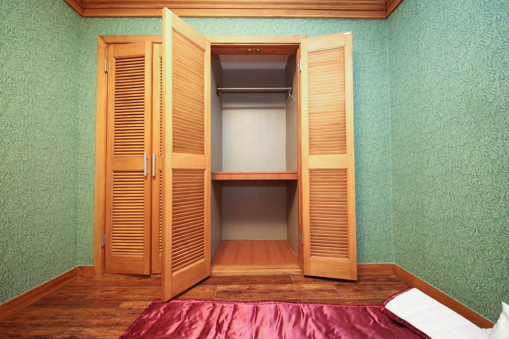 A room with a wooden wardrobe, a bed with a pink bedspread, and green patterned wallpaper.