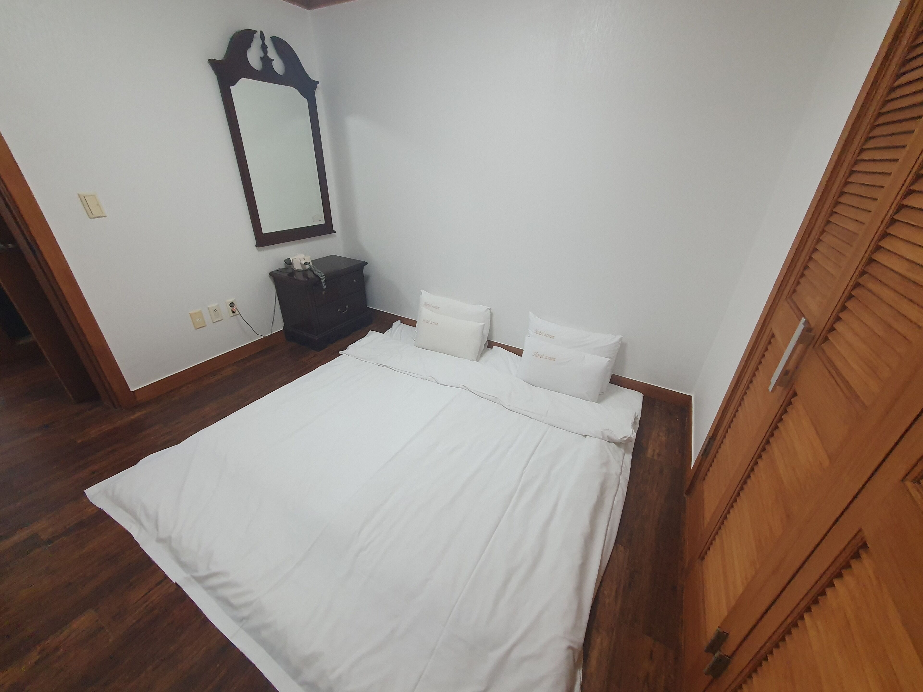 A bedroom with a bed, a nightstand, a mirror, and a wardrobe.