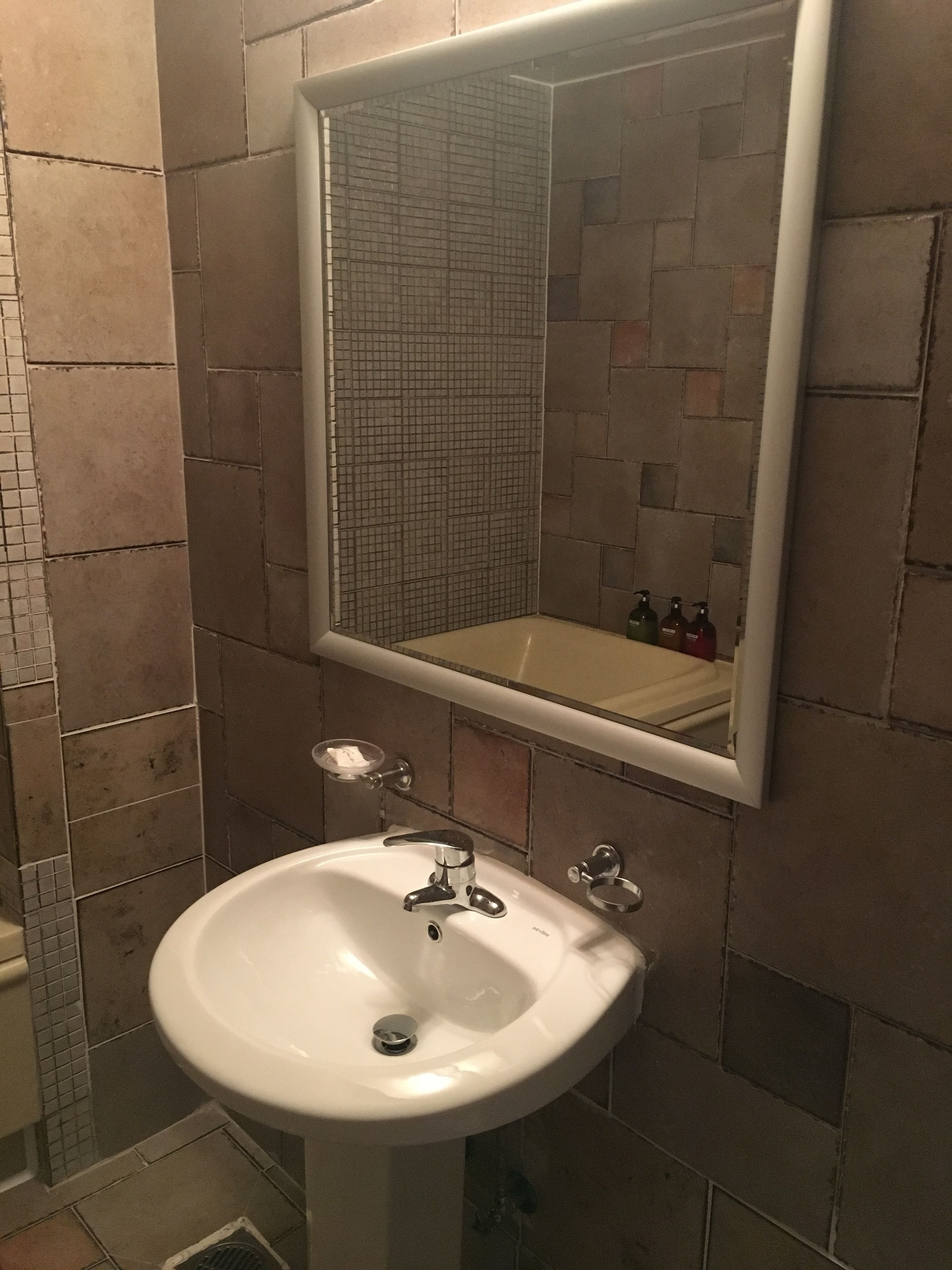 Um banheiro com pia branca, espelho e parede revestida de azulejos.