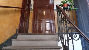 Une porte en bois, située en haut d’un escalier orné d’une rampe en métal, avec un pot de fleurs placé à côté.