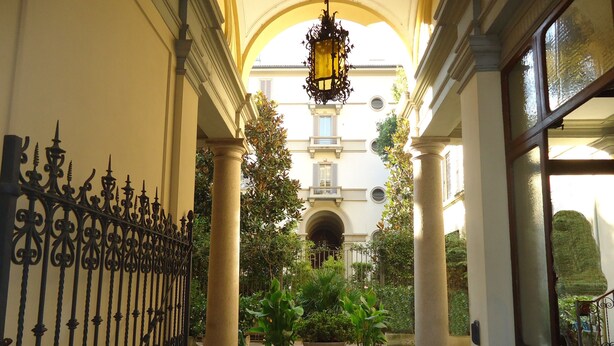 Un couloir orné de colonnes, de plantes en pot et d’une lanterne suspendue.
