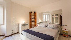 Une chambre à coucher comprenant un lit, des tables de chevet, une armoire, un miroir et une étagère avec des objets décoratifs.