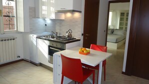 Une cuisine compacte équipée d’une cuisinière à gaz, d’un four et d’un évier. Une table à manger avec des chaises est placée à proximité de la cuisine.