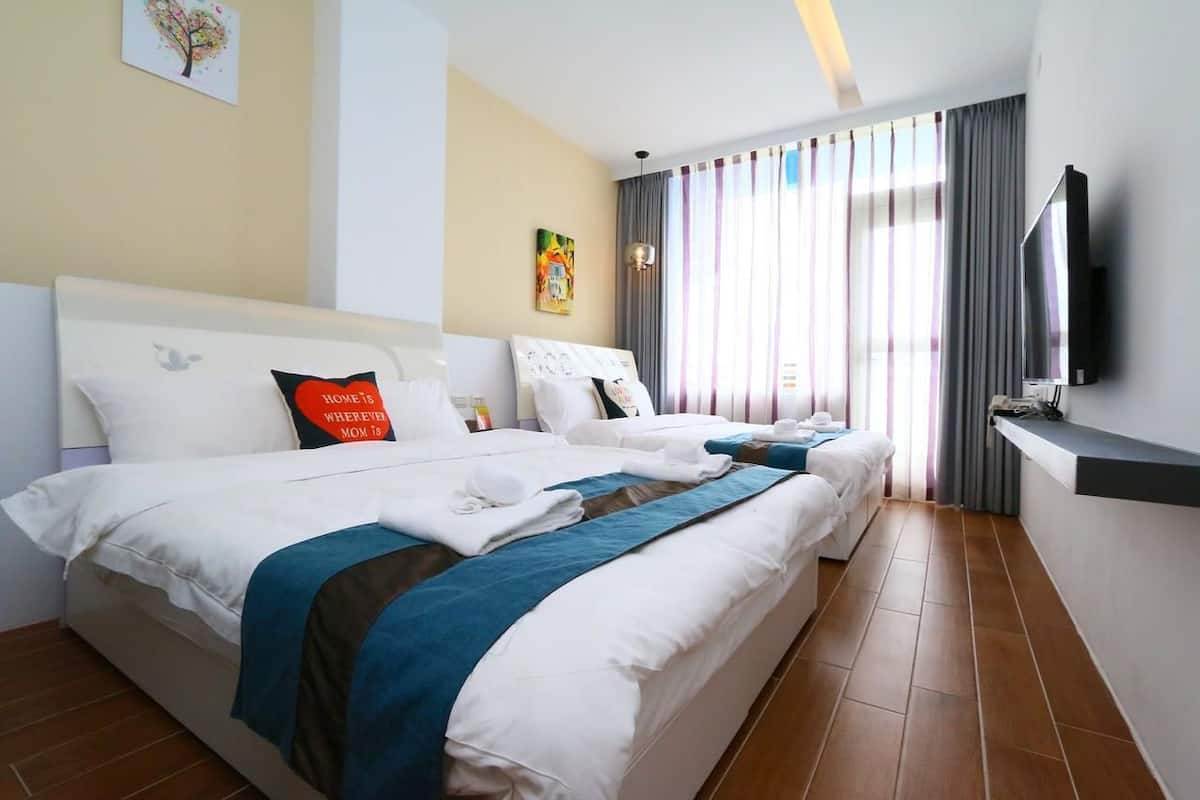 A hotel room with two beds, a TV, and a large window with curtains.