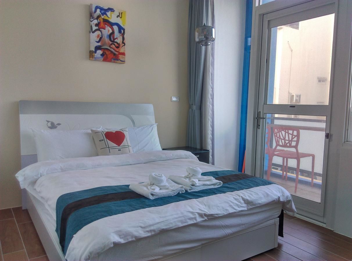 A hotel room with a bed, a painting on the wall, and a view of the outside balcony.