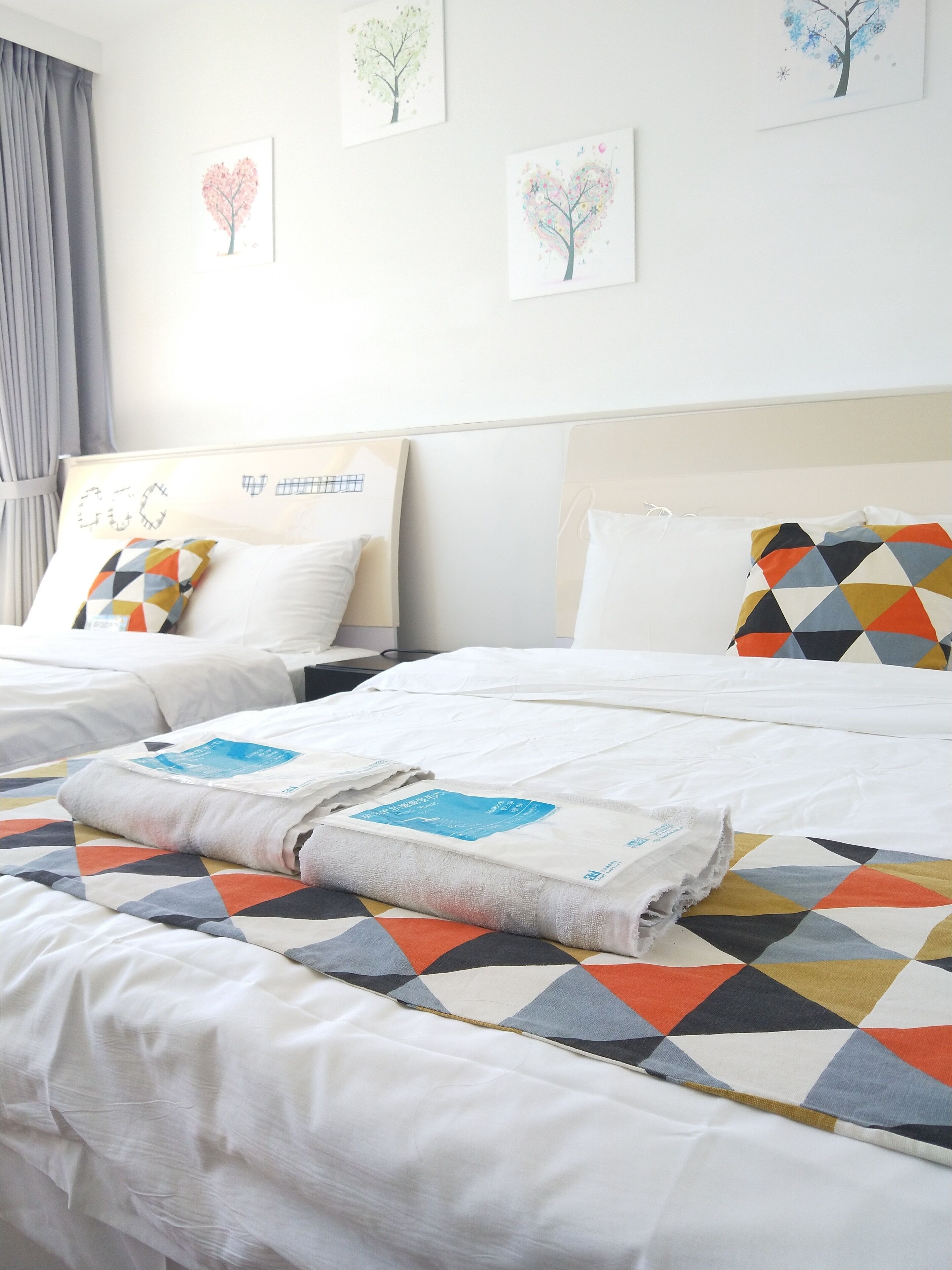 Quarto de hotel com duas camas, cada uma com um design de almofada diferente, e uma parede com três obras de arte emolduradas.