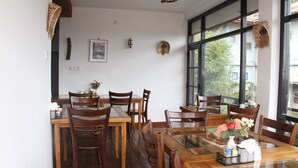 A dining area with wooden tables and chairs, a glass-top table, and a vase with flowers. - chez allen (Nuwara Eliya)