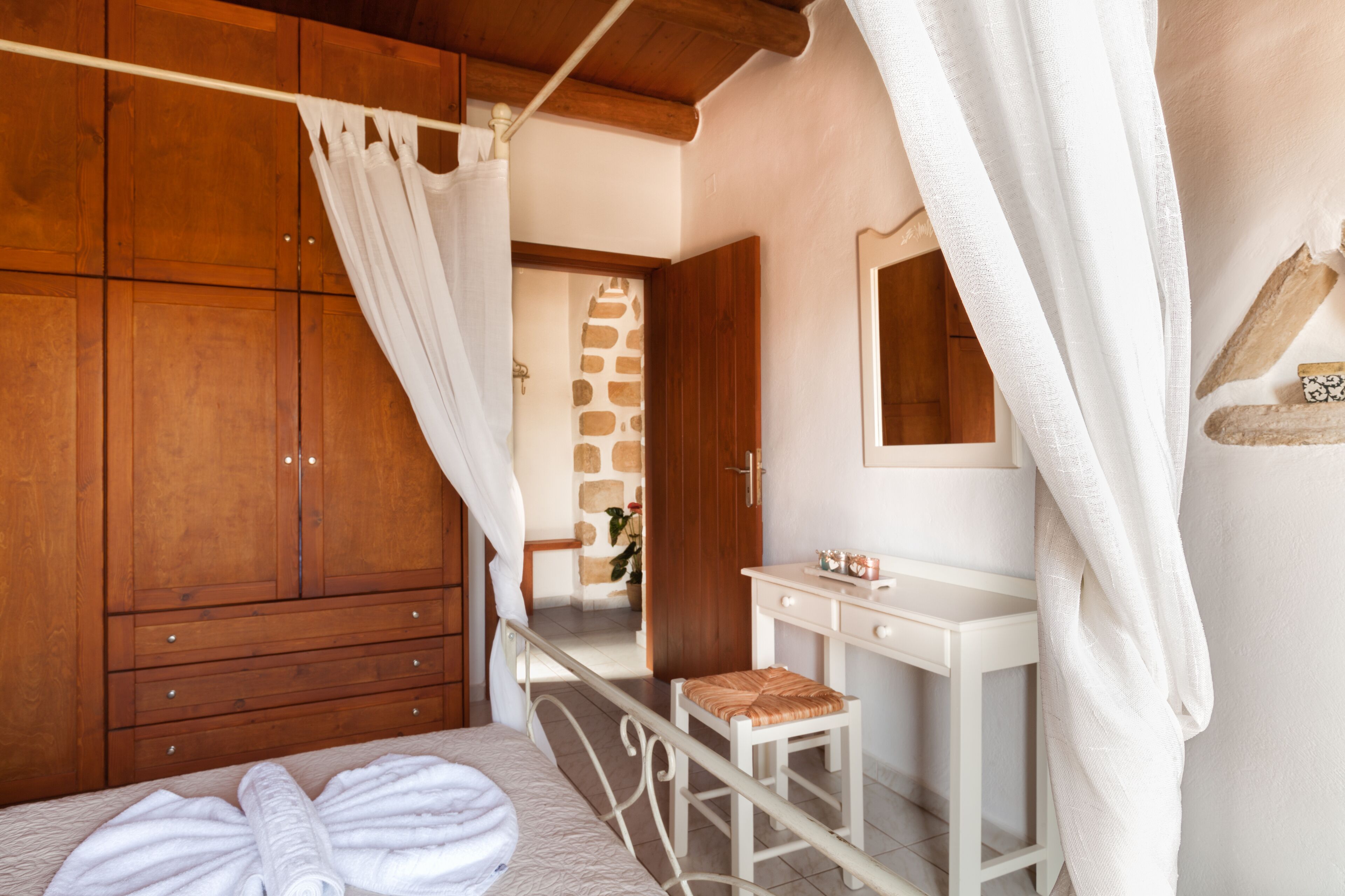 Une chambre à coucher avec une armoire en bois, une table de chevet blanche, un miroir et un lit à baldaquin.