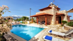 Ein Pool mit Liegestühlen und ein Gebäude mit Steinbauweise und einem Ziegeldach.