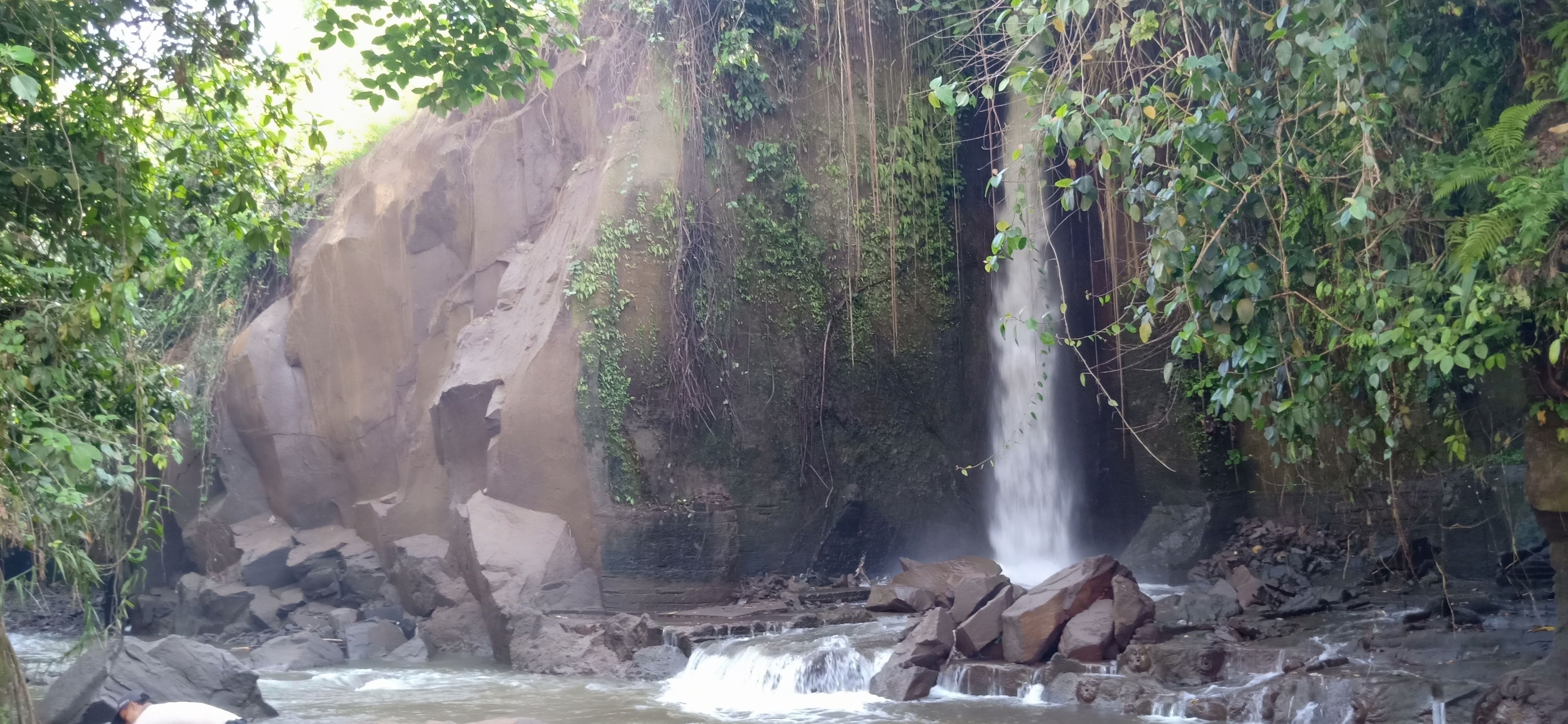 Una cascada que desciende sobre rocas en un entorno natural con vegetación densa.