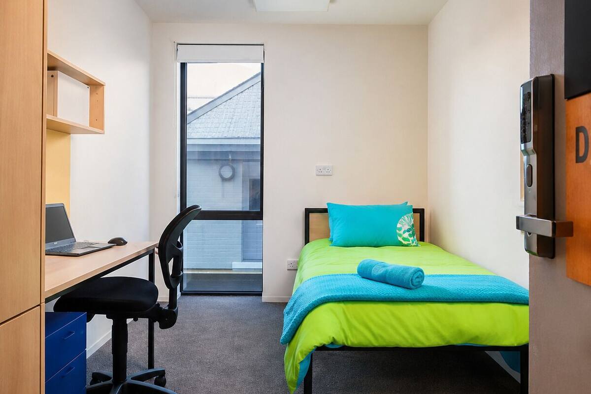 Ein Schlafzimmer mit einem Bett, einem Schreibtisch mit Stuhl, einem Fenster und einer Tür.