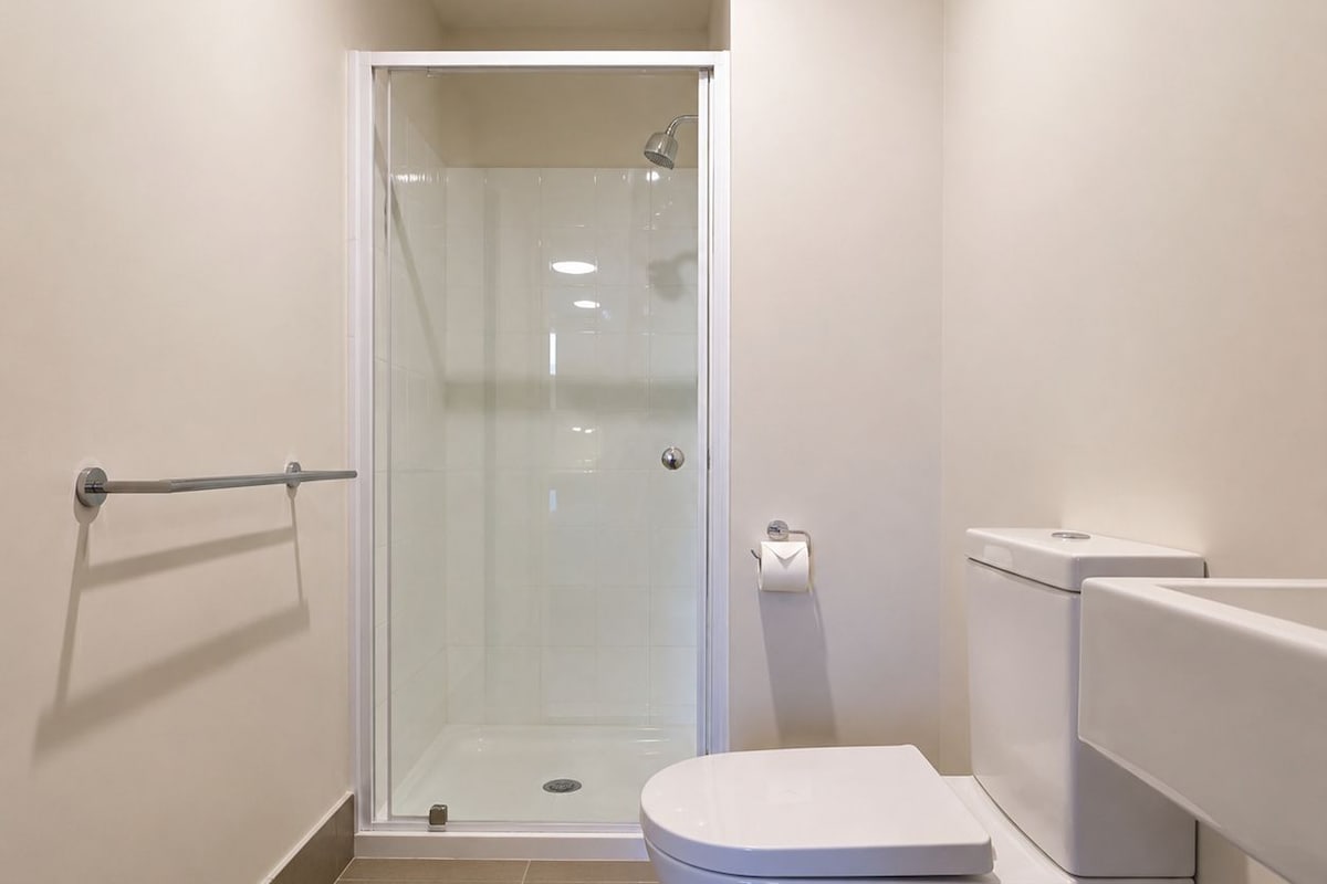 Une salle de bain moderne avec une douche à parois de verre, des toilettes blanches et un porte-rouleau de papier toilette visible.