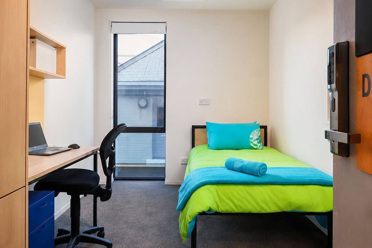 Une chambre à coucher avec un lit, un bureau avec une chaise, une fenêtre et une porte.