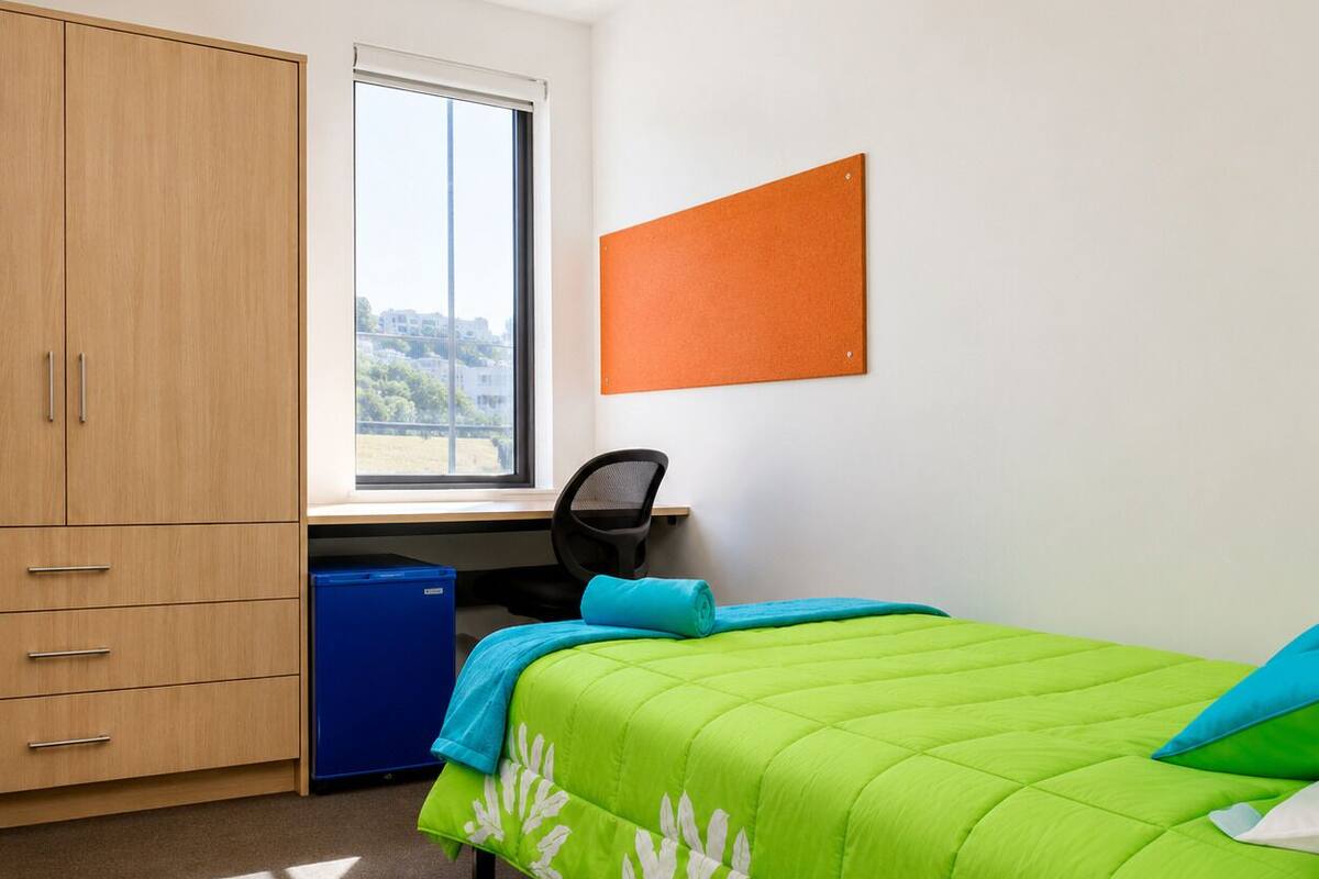 Ein Schlafzimmer mit Bett, Schreibtisch, Stuhl, Kleiderschrank und Fenster.