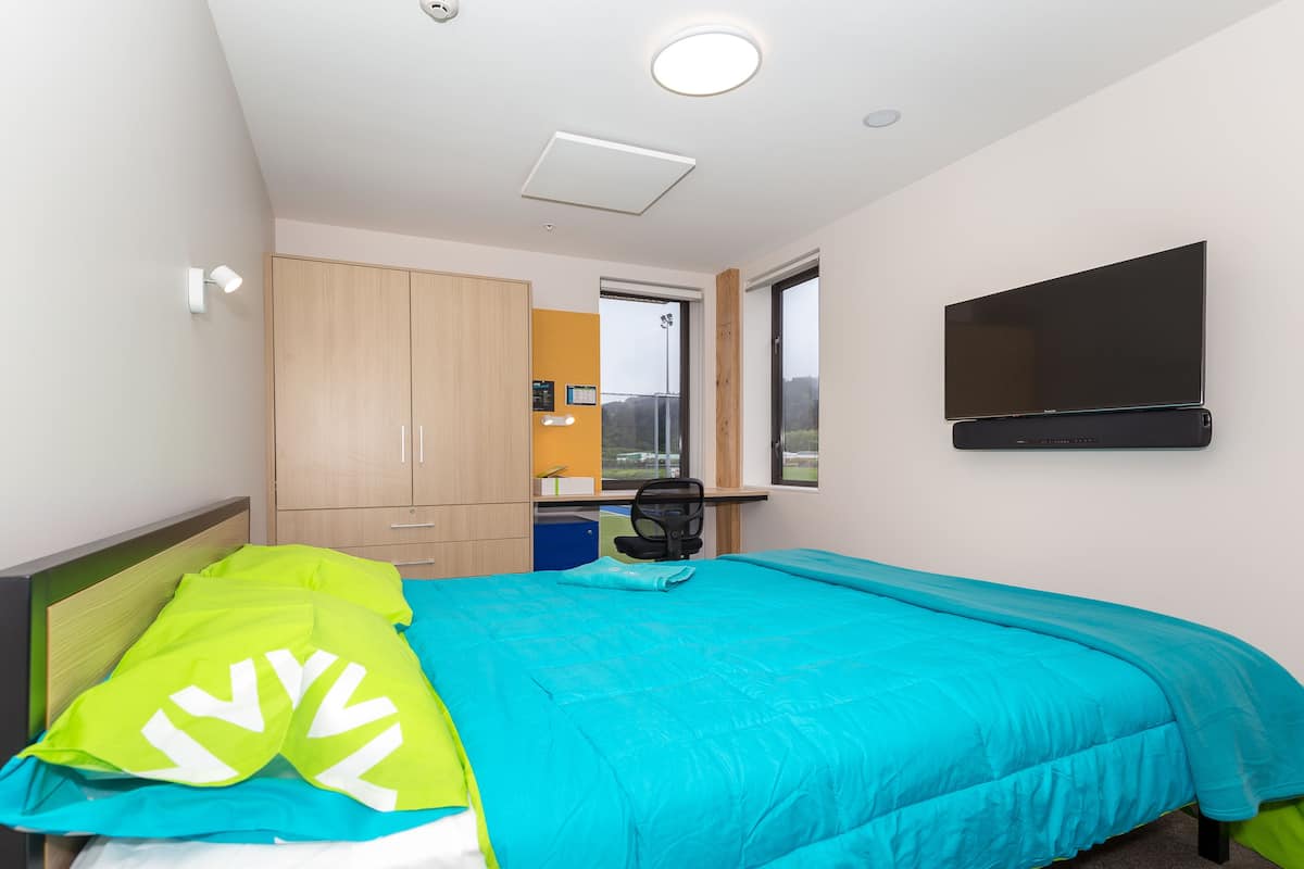 Ein Schlafzimmer mit einem Bett, einem Schreibtisch, einem Sessel, einem Fernseher und einem Kleiderschrank.