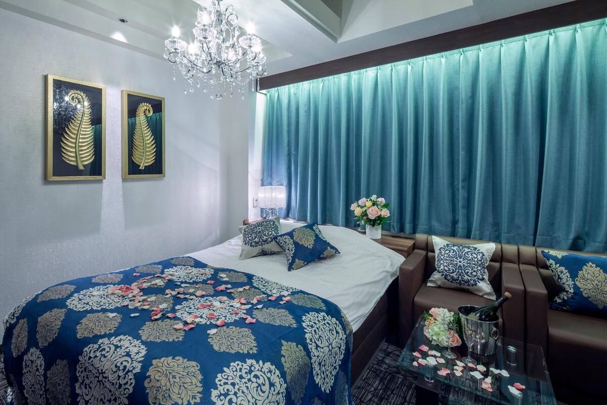 Quarto com cama, sofá, mesa de centro de vidro, lustre e cortinas.