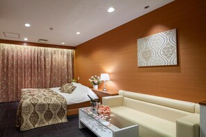 A hotel room with a bed, a sofa, a coffee table, a lamp, and a wall-mounted artwork. - Restay Hiroshima - Adult Only (Hiroshima)