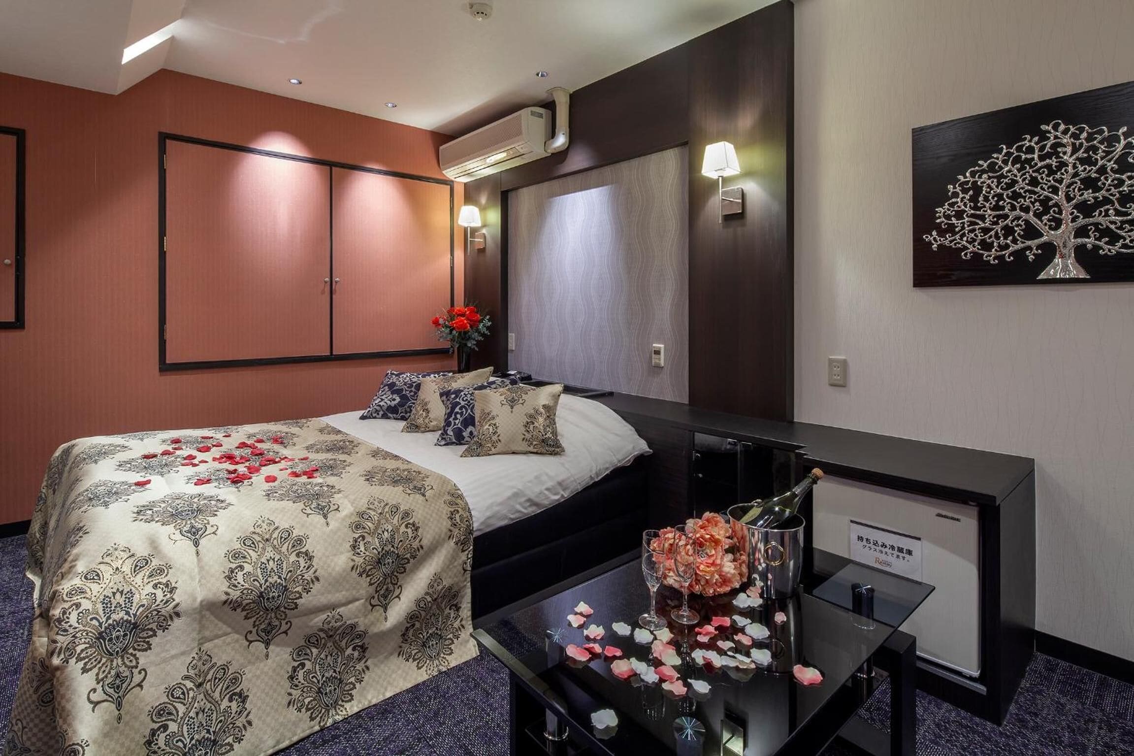 Una habitación de hotel con una cama, un escritorio con una botella de champán y un florero con flores.