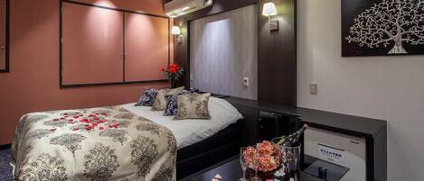 Una habitación de hotel con una cama, un escritorio con una botella de champán y un florero con flores.