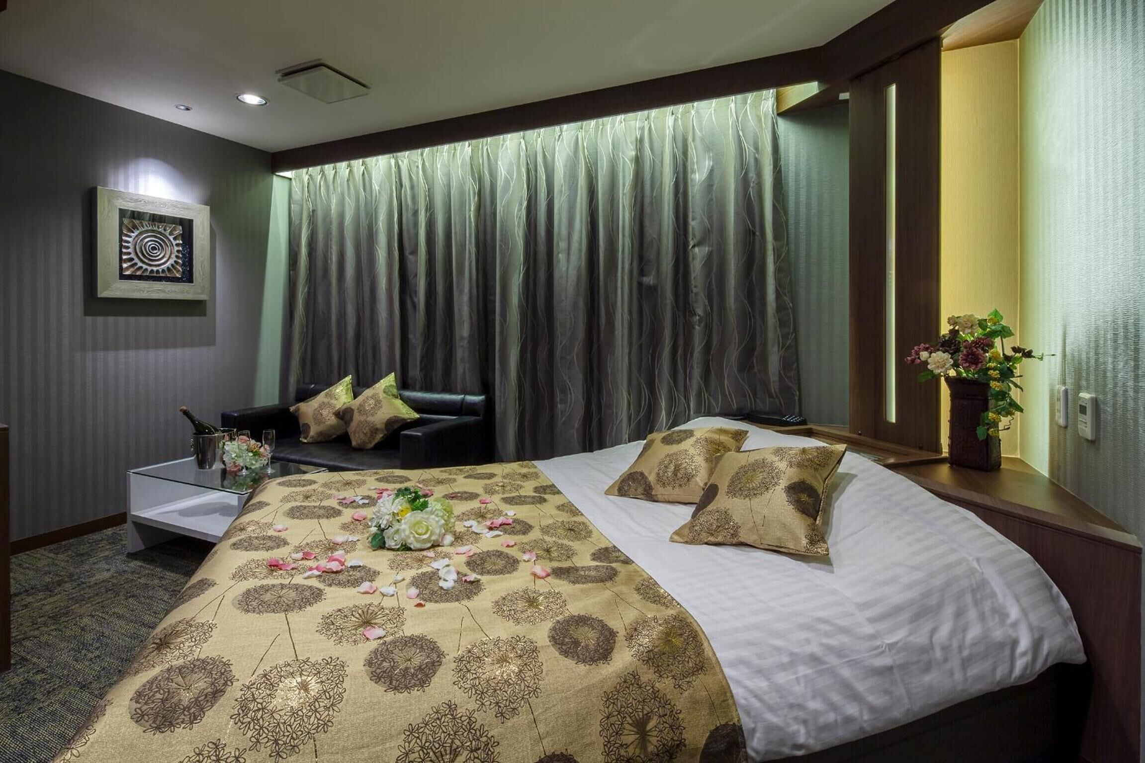 A hotel room with a bed, a nightstand, a chair, a curtain, and a wall-mounted artwork.