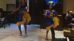 Dos bailarines con trajes coloridos actuando en una sala con piso de baldosas e iluminación en el techo.