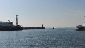 Un port où est amarré un grand navire, un phare et, au loin, un pont.