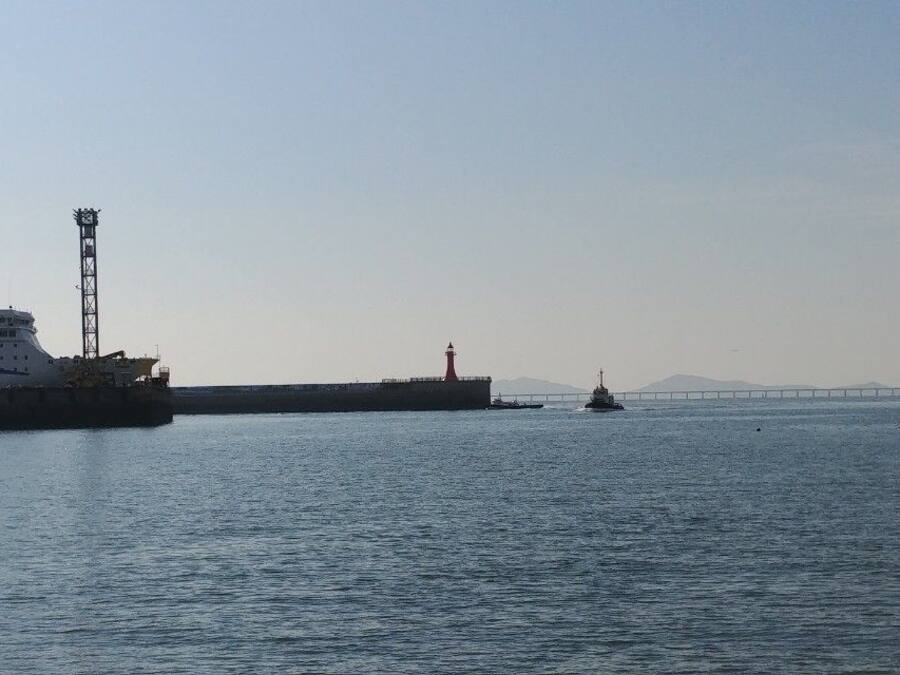 Un port où est amarré un grand navire, un phare et, au loin, un pont.