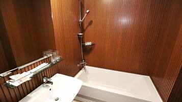 A modern bathroom with a white bathtub, a glass shelf with toiletries, and a wooden panel wall.