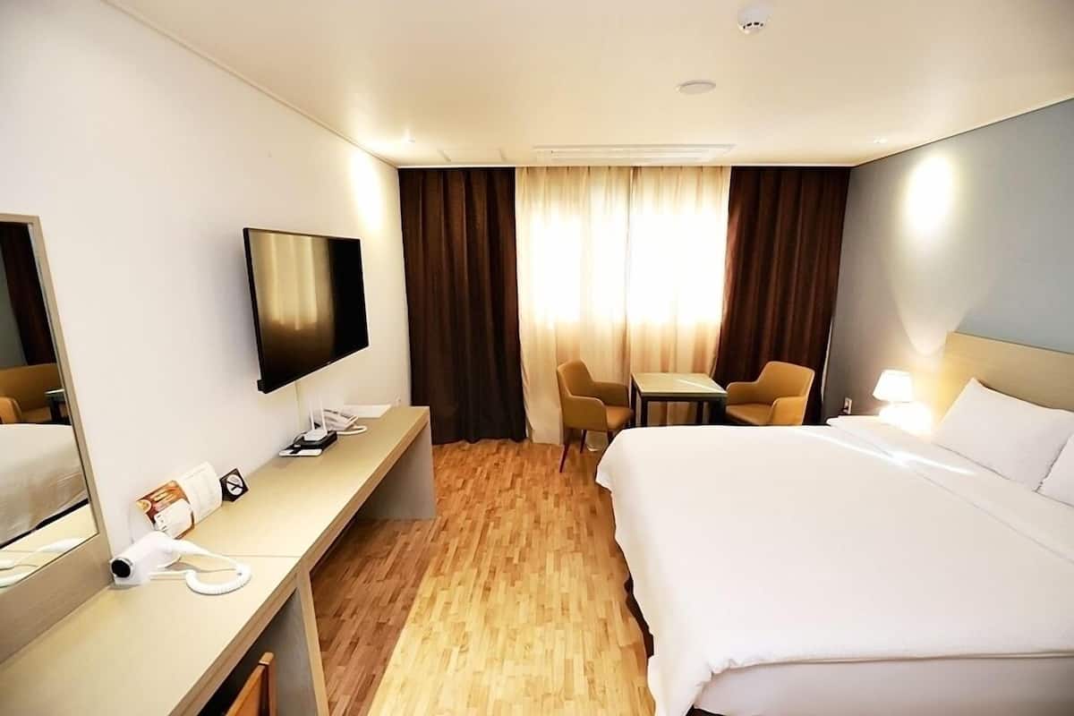 A hotel room with a bed, a desk with a telephone, a television, a chair, and a table.
