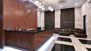 A modern reception area with a wooden reception desk, black and white tiled flooring, a brown leather sofa, and a decorative light fixture. - Sea & Moon Tourist Hotel (Incheon)