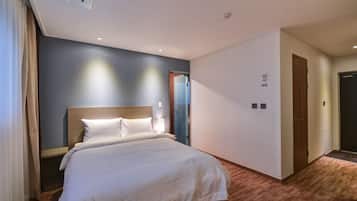 A hotel room with a large bed, a wooden headboard, a nightstand, and a bedside lamp.