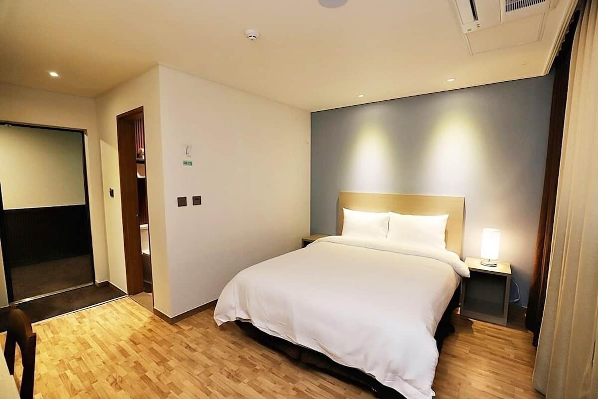 A hotel room with a large bed, a bedside table with a lamp, and a wardrobe.