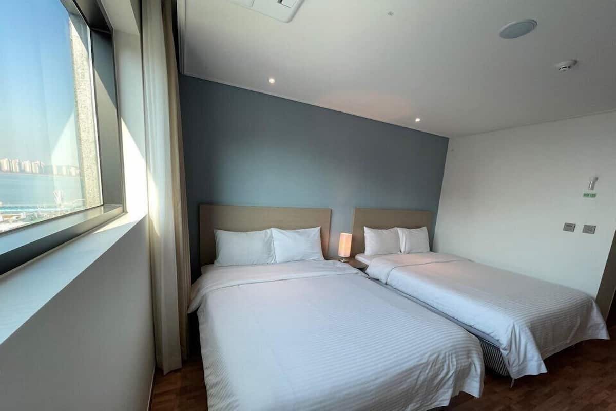 A hotel room with two beds, a large window, and a view of the sea.