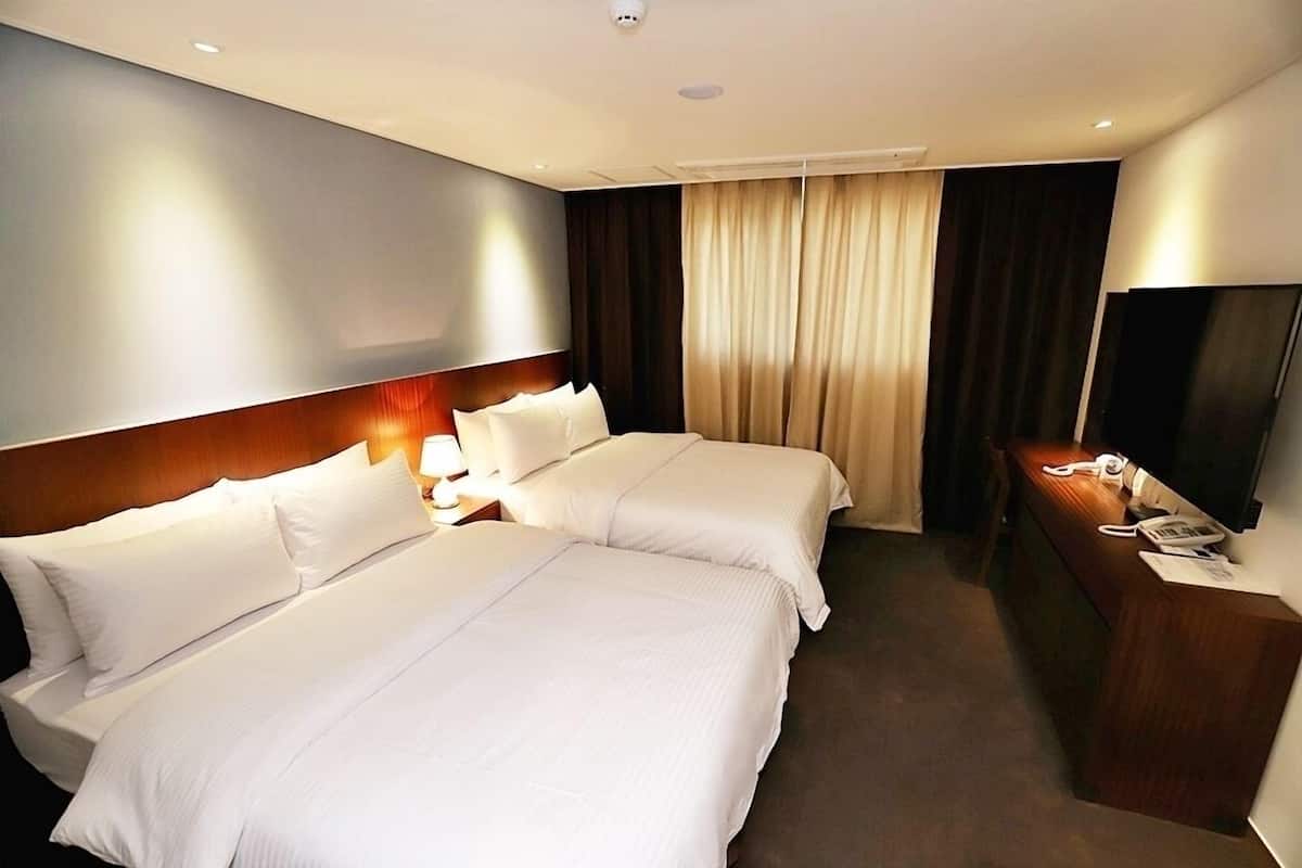 A hotel room with two beds, a desk, a TV, and a window with curtains.
