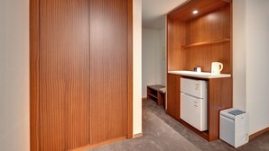 A compact room with a wooden wardrobe, a small kitchenette with a refrigerator and a coffee maker, and a bench. - Sea & Moon Tourist Hotel (Incheon)