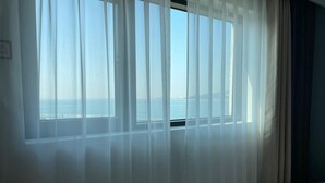 A hotel room with a large window covered by sheer curtains, a bed, and a view of the sea. - Sea & Moon Tourist Hotel (Incheon)