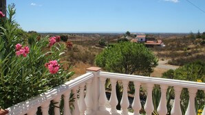 Un balcone con ringhiera bianca che si affaccia su un paesaggio rurale con una casa e della vegetazione.