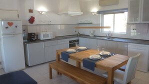 Una cucina moderna con mobili bianchi, un tavolo da pranzo in legno apparecchiato con piatti e bicchieri, un forno a microonde e un frigorifero decorato con un magnete a forma di cuore.