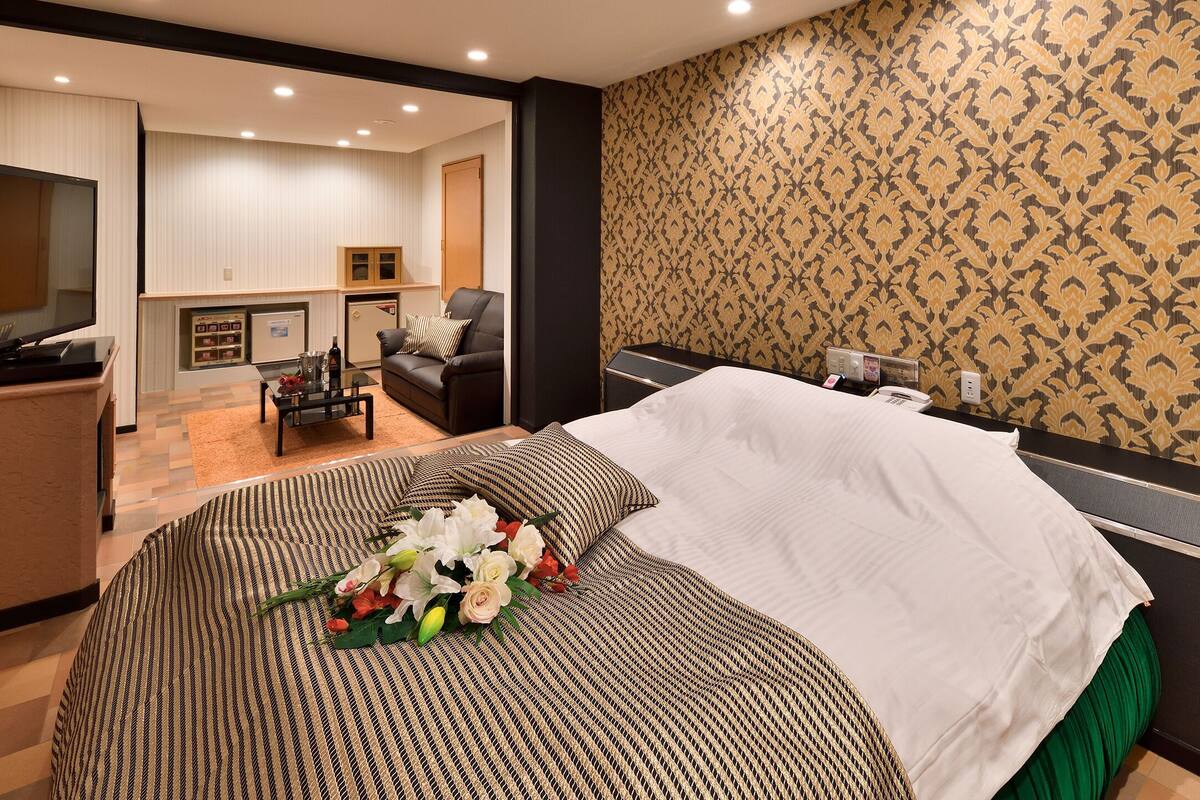 A hotel room with a bed, a TV, a small kitchenette, and a patterned wallpaper.