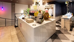 Zona de recepción de un hotel con un mostrador que exhibe diversos servicios, un letrero que dice 'Alquiler' y una escalera.