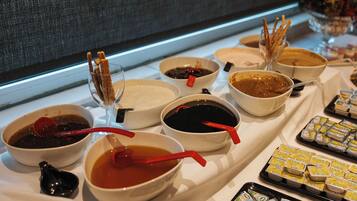 A buffet table with various dishes and condiments, including bowls of soup and sauces, and trays of packaged food.