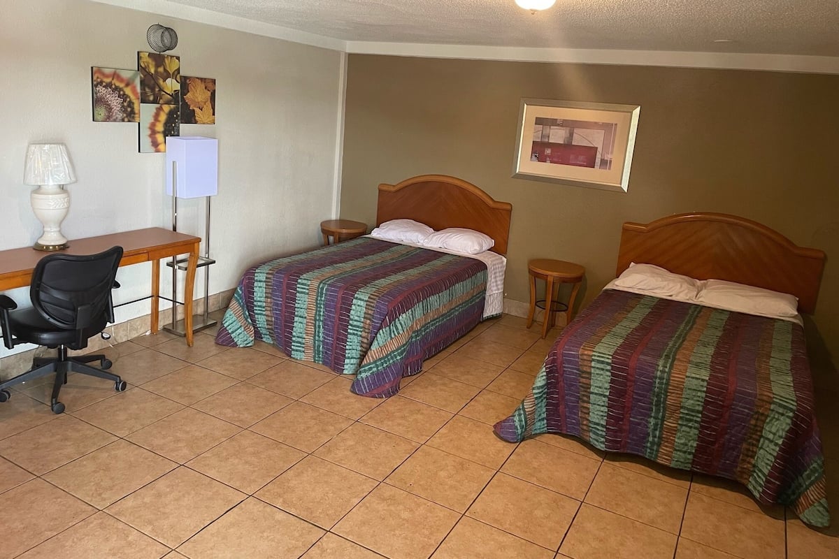 Una habitación con dos camas, un escritorio, una silla y una lámpara.